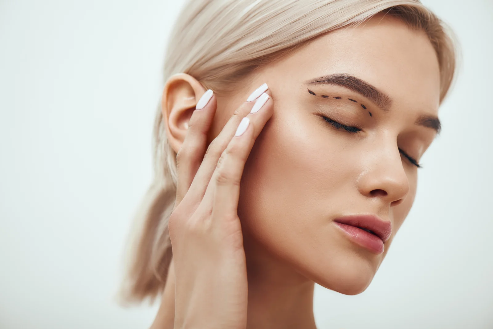 Woman touching her face near the eye area, demonstrating blepharoplasty treatment zone